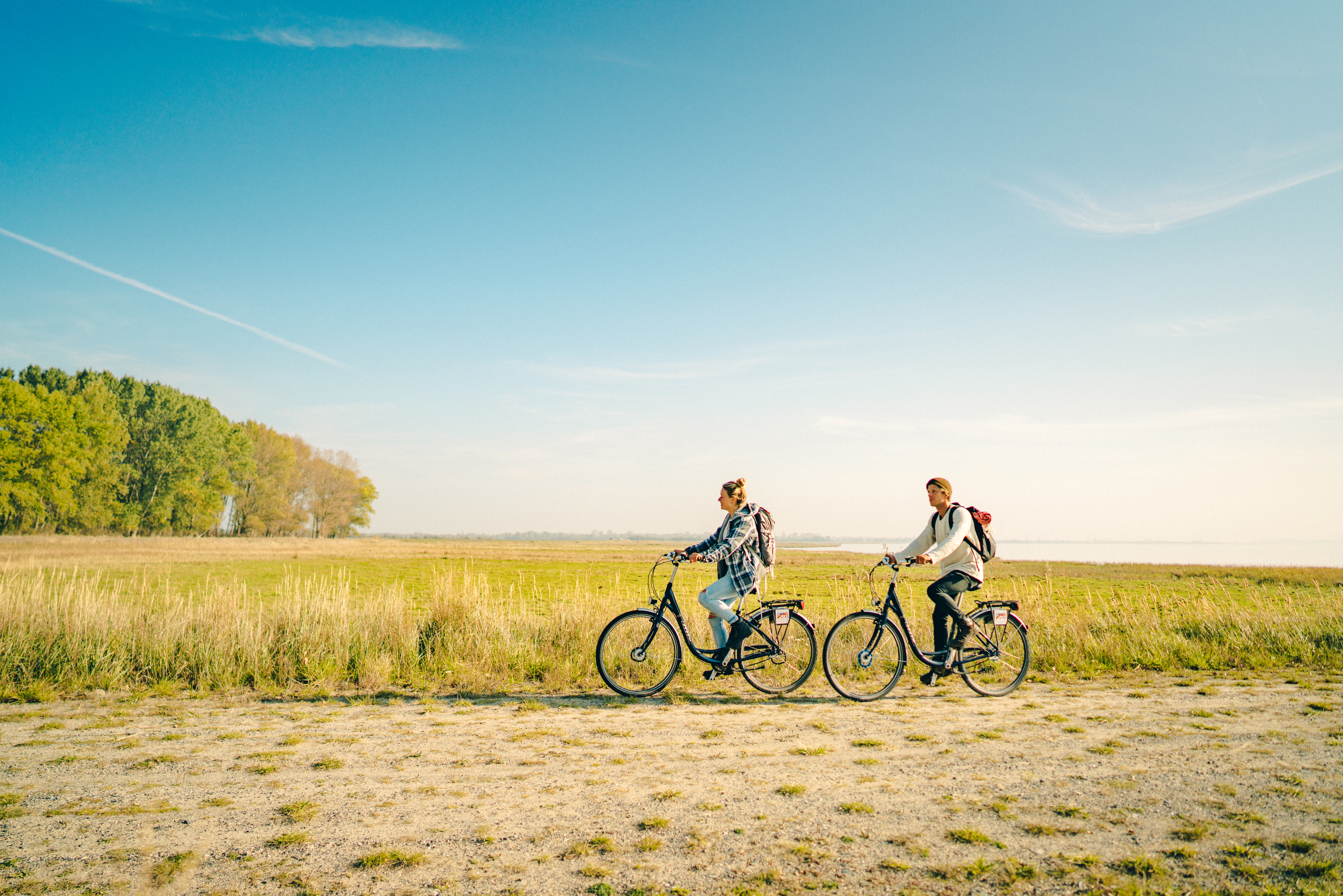 Zwei Radfahrer, ein Mann und eine Frau, fahren hintereinander einen Feldweg entlang